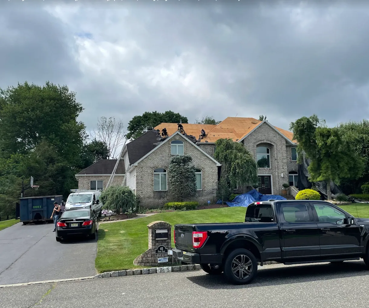 The AAA Apex crew re-roofing a large brick home in New Jersey, with new plywood decking going down and the property tarped