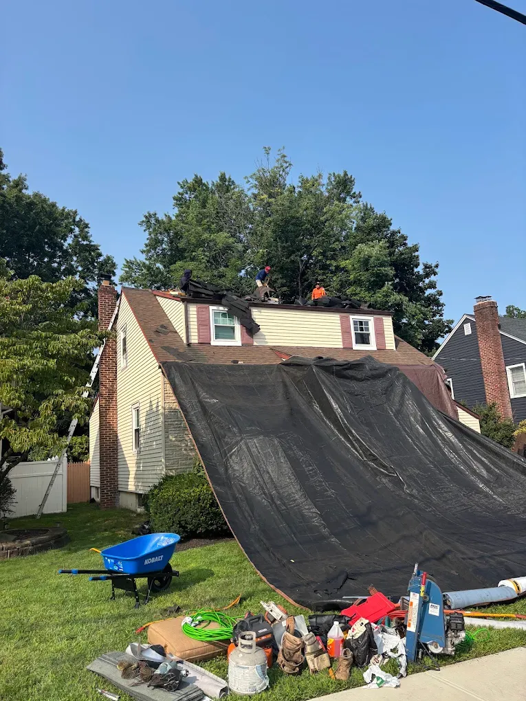 A catch tarp hung from a roof over the lawn and shrubs during a tear-off