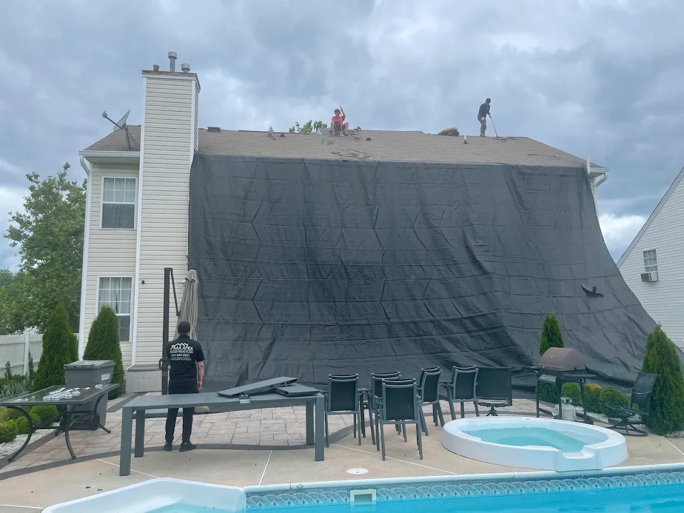 An AAA Apex roofer beside a catch tarp hung from the roof to protect the patio and pool during a tear-off