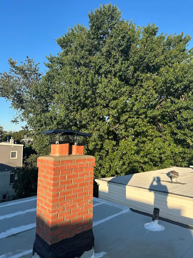 A brick chimney with a new cap rising from a freshly coated flat roof at sunset