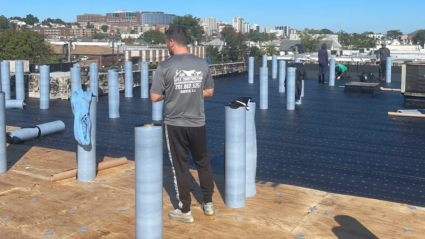 Rolls of roofing membrane standing upright on a large flat roof with a city skyline behind