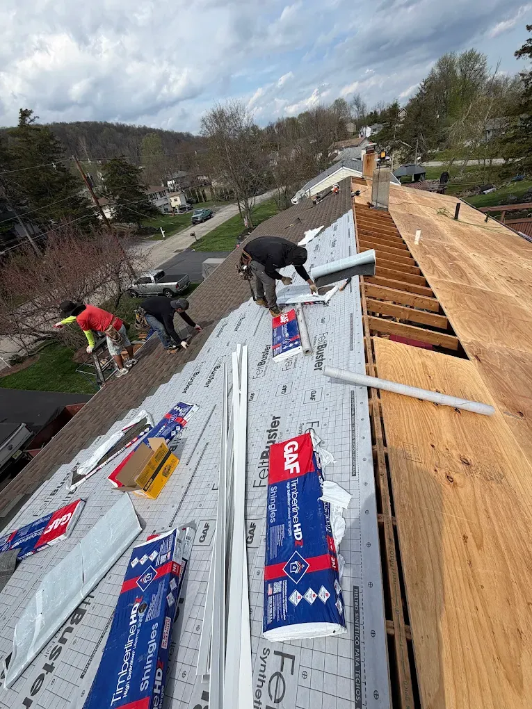 Roofers installing synthetic underlayment and shingles on a hillside home