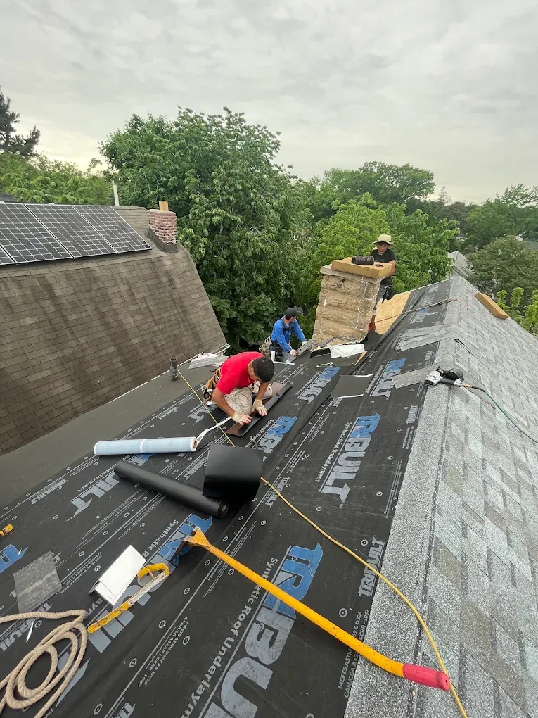 Roofers laying underlayment around a chimney next to solar panels