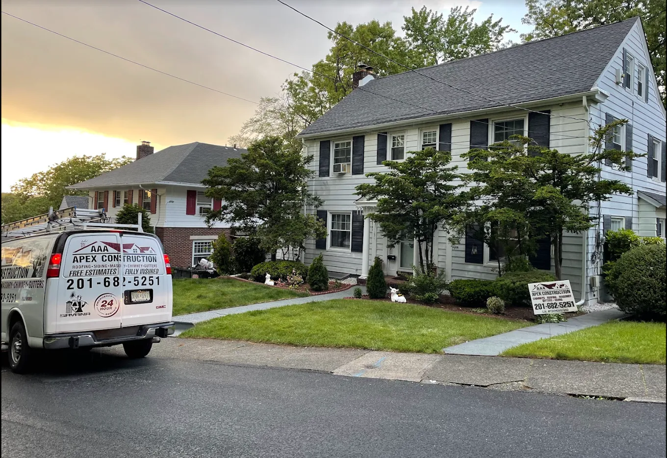 A white colonial house with a new dark shingle roof at dusk, with the AAA Apex van parked out front