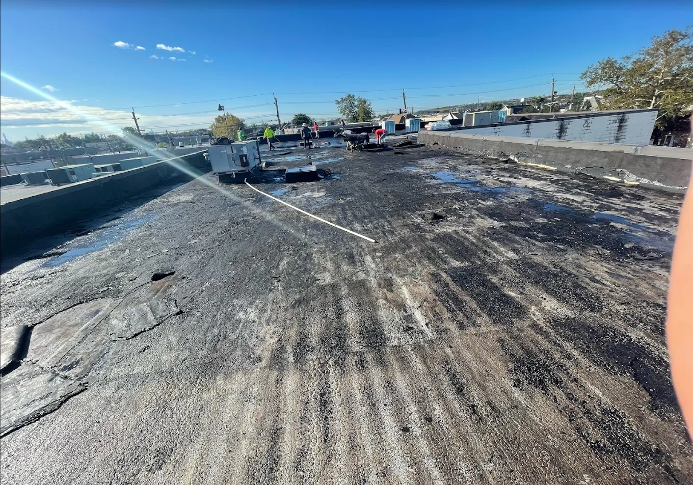 A worn, patched flat commercial roof under a blue sky
