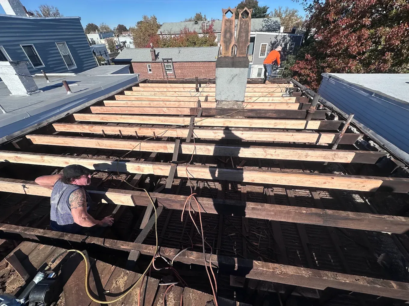 A roofer setting new wood joists on an opened flat roof between row houses