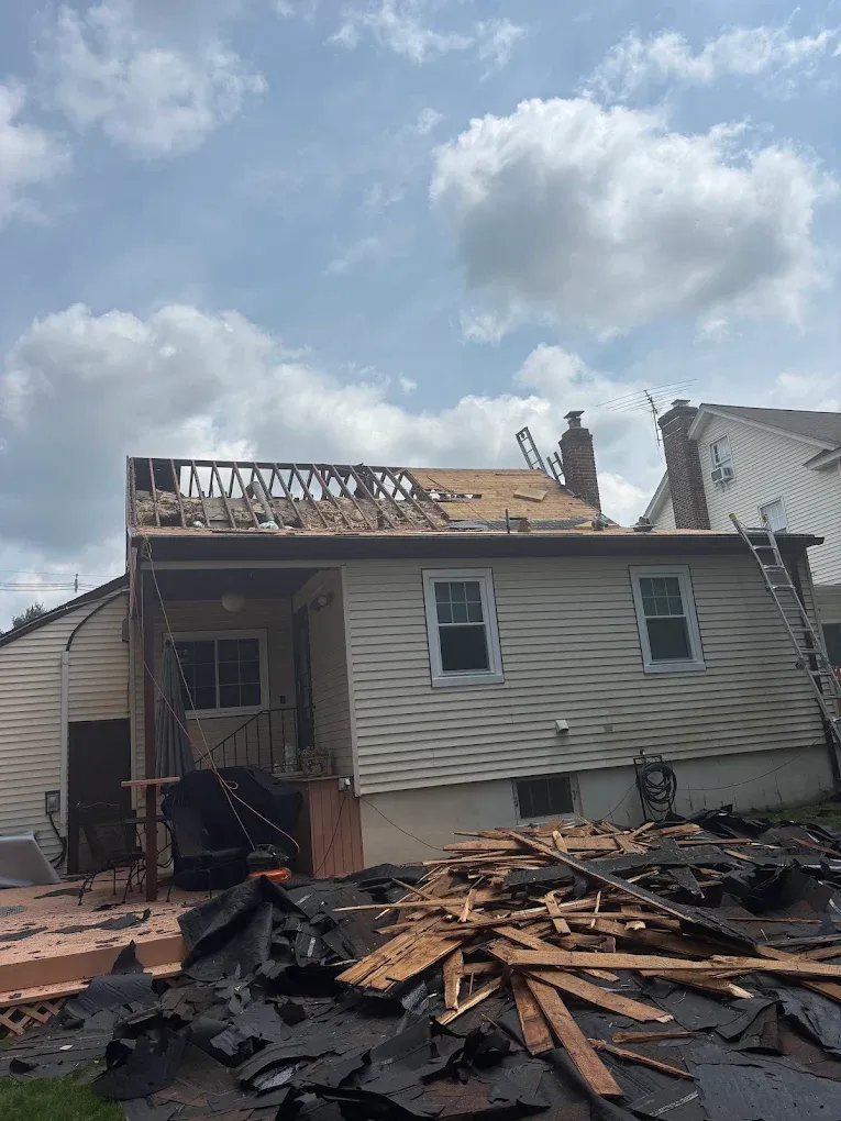 A house with its roof stripped down to bare rafters and debris in the yard