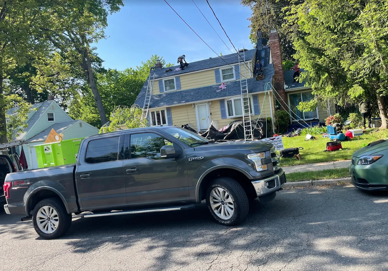 A roofer on a yellow colonial house with a pickup truck in the foreground